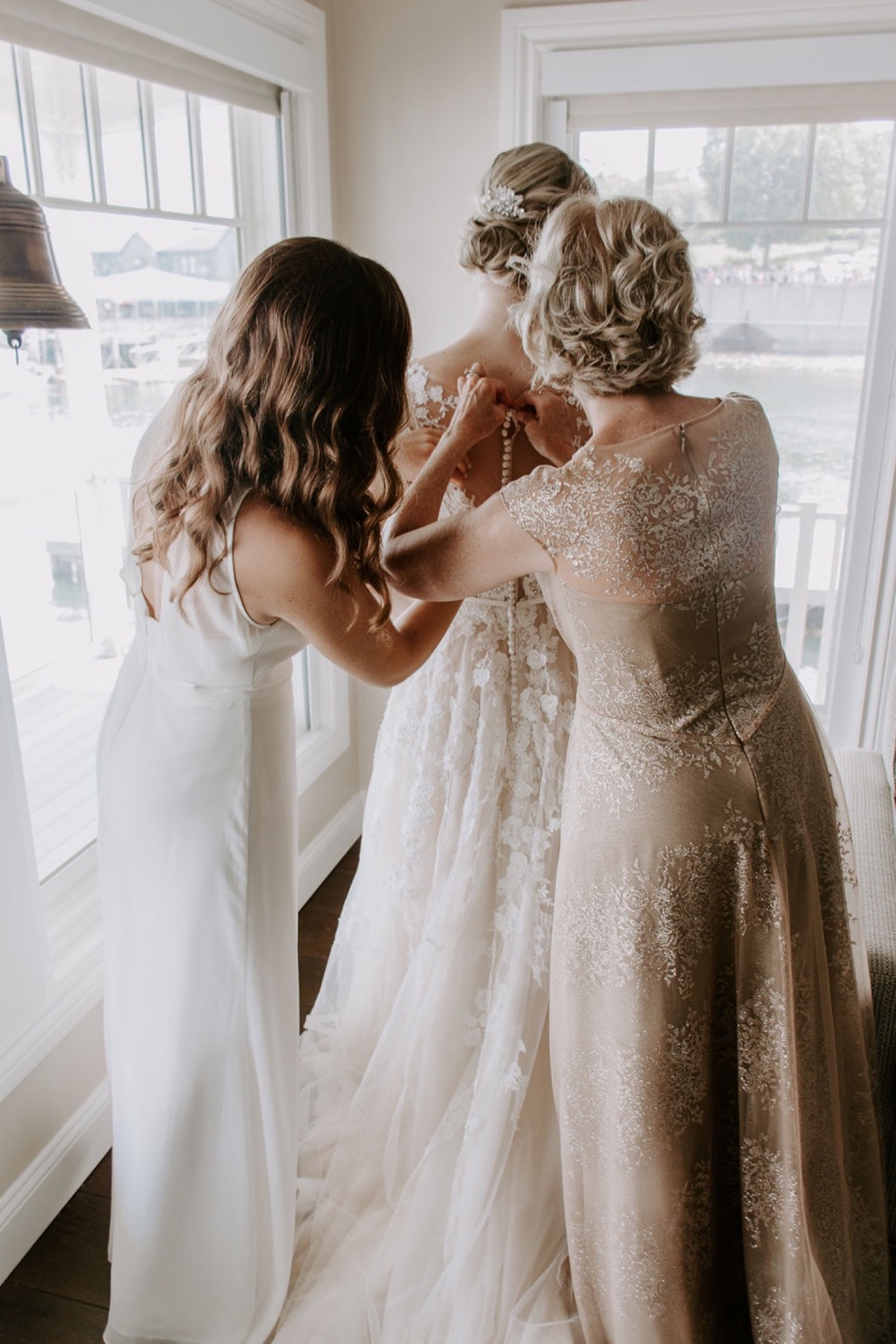 mother and bridesmaid doing up buttons on bride's dress