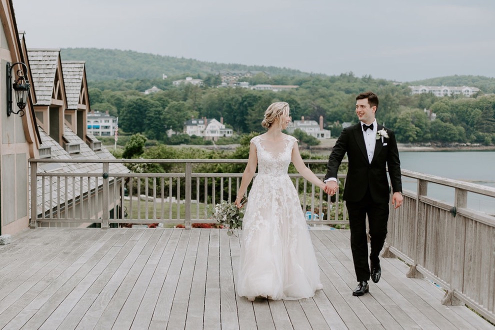 bride and groom hold hands as they walk along balcony overlooking ocean