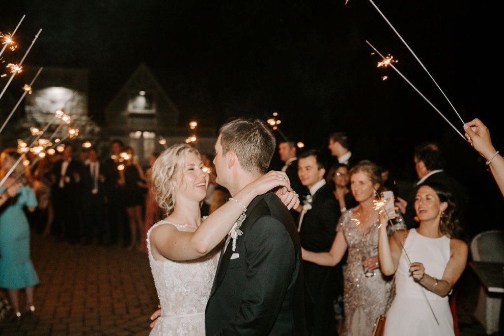 bride and groom smile as guests hold sparklers overhead