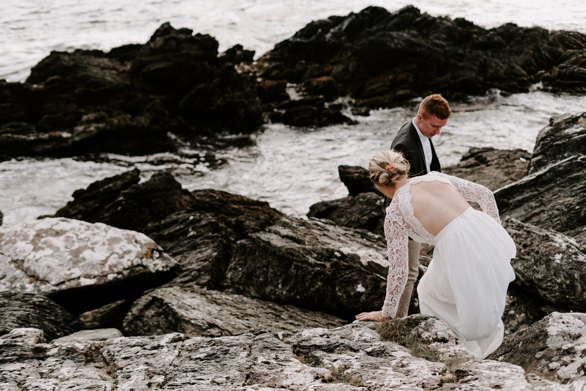 bride and groom climbing over rocks as tide comes in
