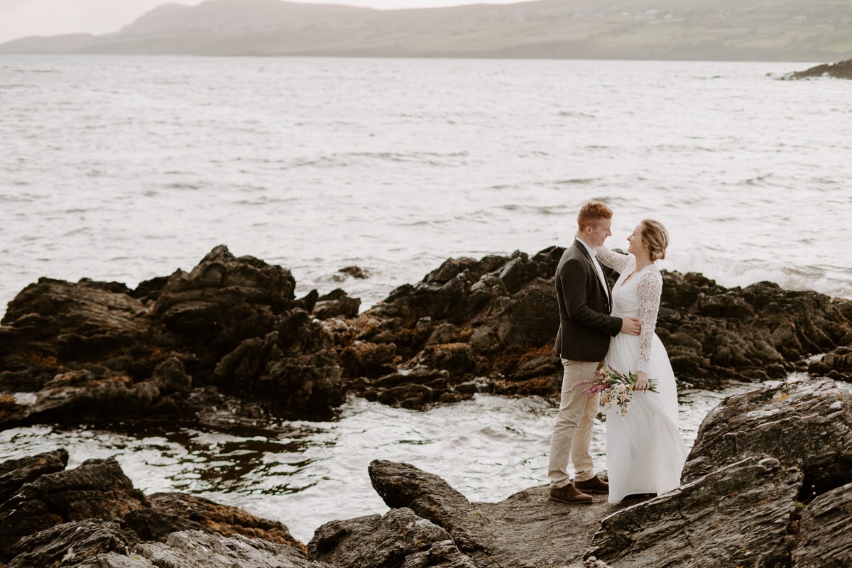 bride and groom standing on rocks near ocean