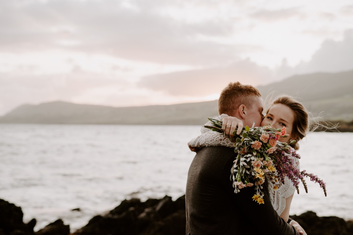 bride and groom embracing near ocean at sunset