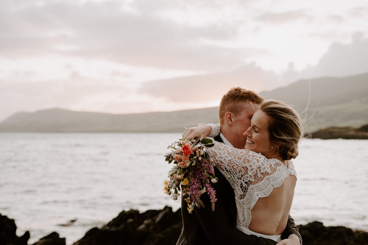 bride and groom embrace at cliffside sunset elopement