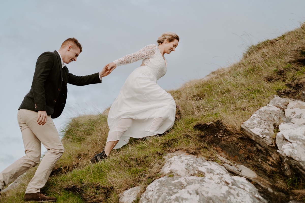 bride and groom run up hillside in Ireland