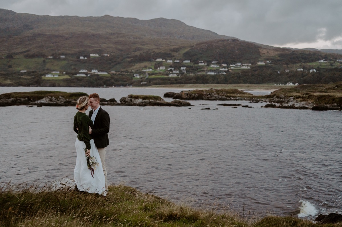 bride and groom stand together with ocean in distance