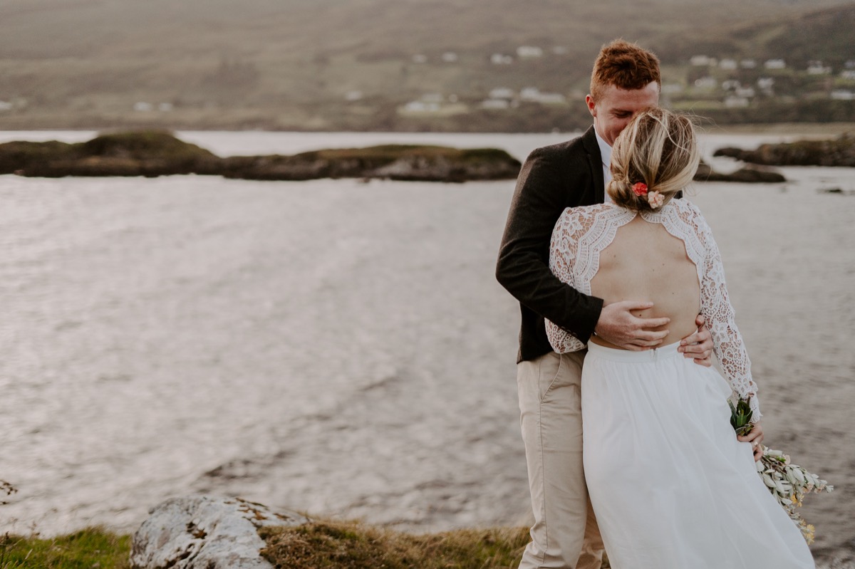 bride and groom laughing at cliff overlooking ocean