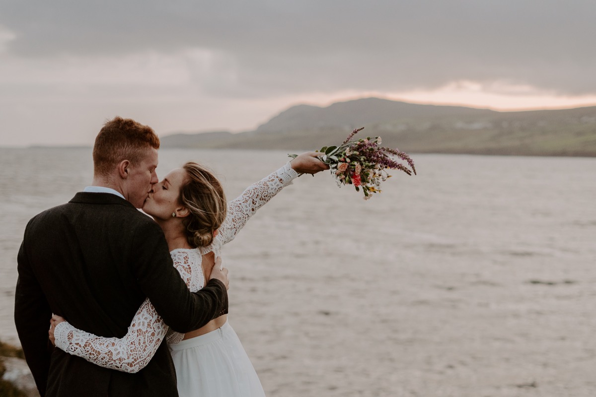 bride and groom triumphantly kissing as sun sets over Irish coast