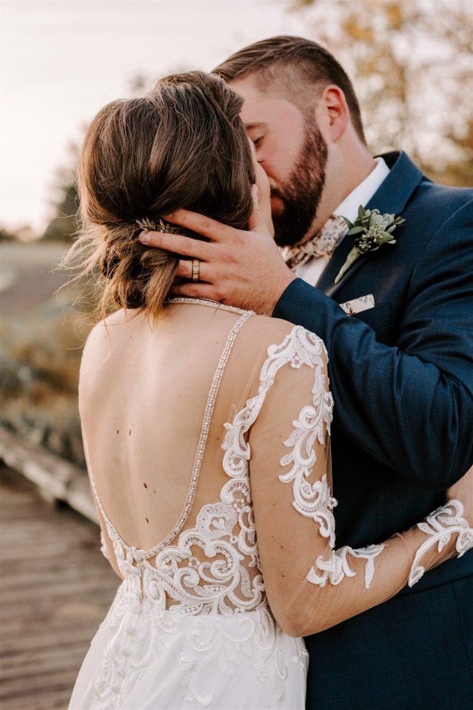 groom kisses bride with low back wedding dress