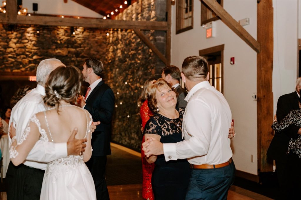 brides mother shares a heartfelt smile with her daughter as she dances with groom while bride dances with her father